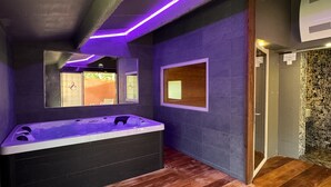 Een moderne badkamer met een groot bad, donkere wanden en een houten vloer.