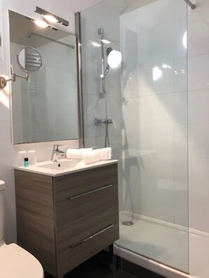 Een moderne badkamer met een douchecabine van glas, een wastafel met spiegel en een toilet.