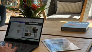 Een laptop op een houten tafel, met een tijdschrift en een smartphone ernaast.