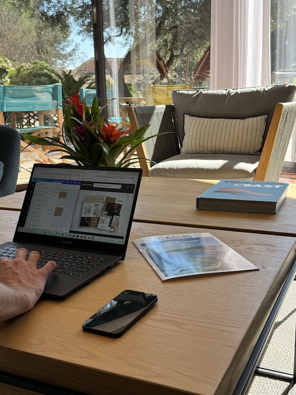 A laptop on a wooden table with a magazine and a smartphone beside it.