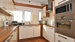 A kitchen with white cabinets, a wooden countertop, a microwave, an oven, and a window. - Lynfield Guest House (Galway)