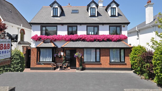 A two-story hotel with a brick facade, large windows, and a balcony with pink flowers. - Lynfield Guest House (Galway)