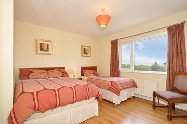A bedroom with two beds, a window with curtains, and a chair.