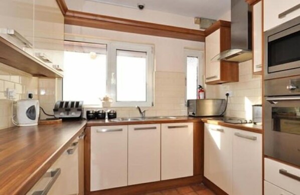 Una cocina moderna con armarios blancos, encimera de madera, horno empotrado y ventana que proporciona luz natural.