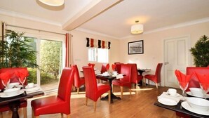 A dining area with red chairs and tables, a large window with curtains, and a door. - Lynfield Guest House (Galway)