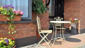 A brick building with a black door, a white table and chair outside, and potted plants with flowers. - Lynfield Guest House (Galway)