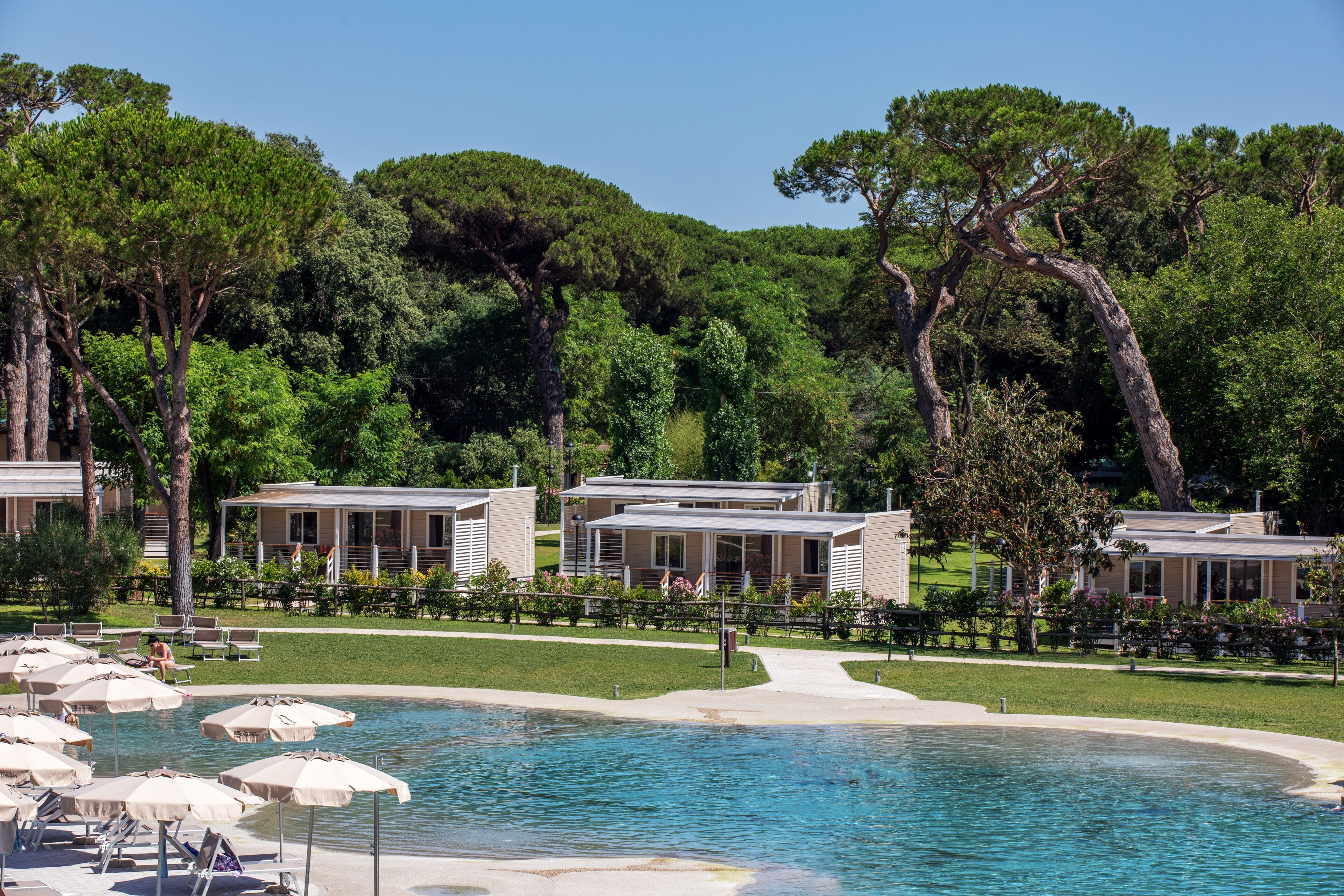 A pool area with lounge chairs and umbrellas, surrounded by trees and buildings.