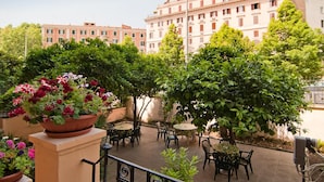 An outdoor patio area with multiple tables and chairs, surrounded by lush greenery and potted plants. - Palma Residences In Rome (Rome)
