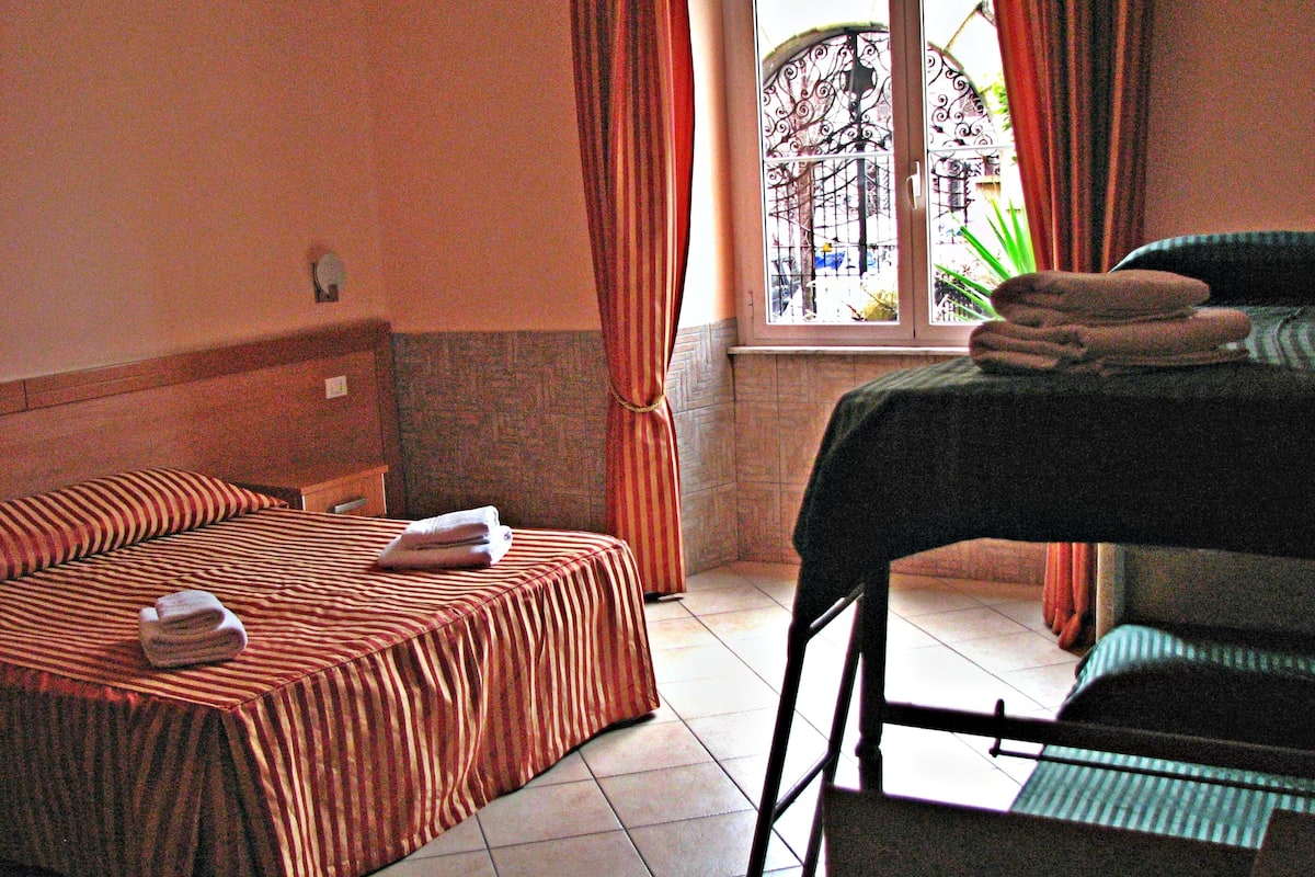 A hotel room with a bed, a chair, and a window with curtains.