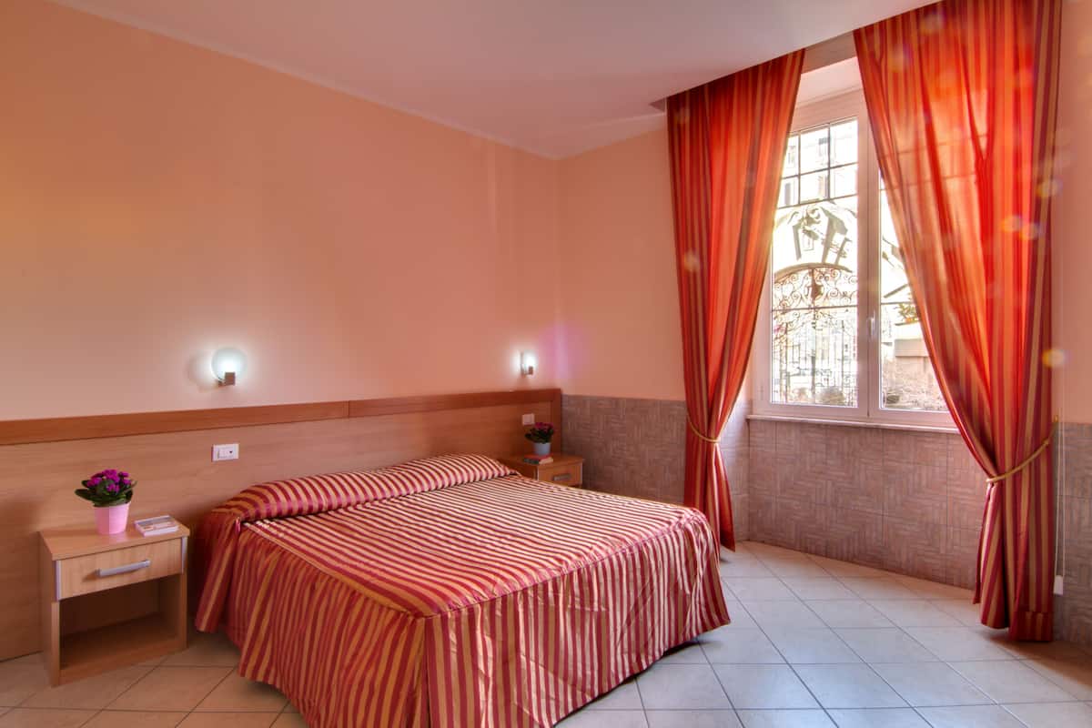 A hotel room with a bed, nightstand, and window with curtains.