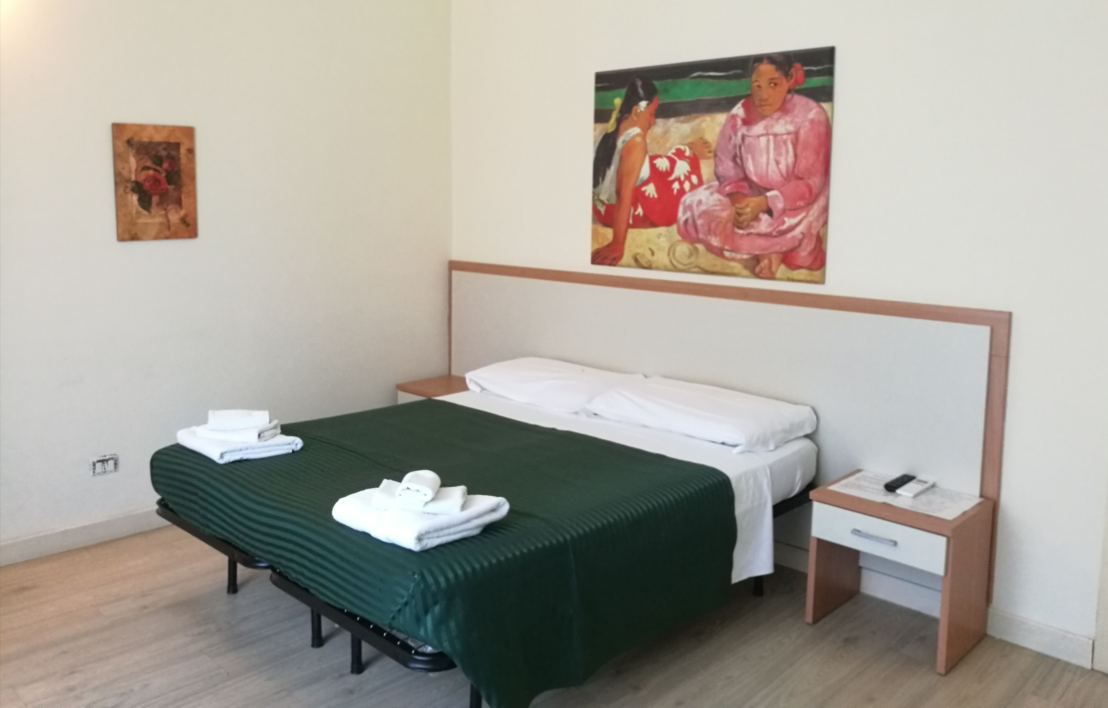 A hotel room with a bed, a nightstand, a drawer, and a painting on the wall.