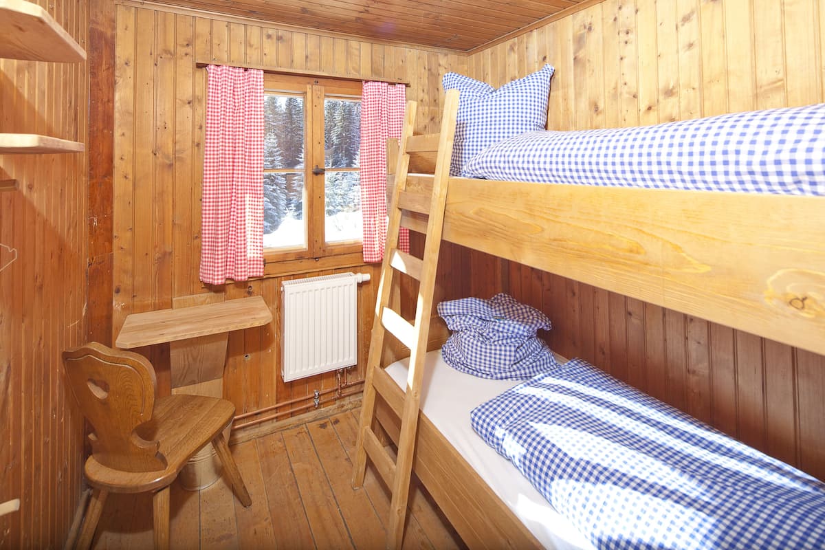 A wooden cabin room with bunk beds, a wooden desk, and a chair.