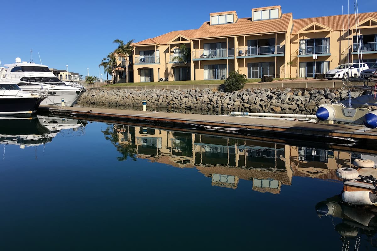 A marina with yachts docked, a stone wall, and a building with balconies.