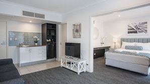 A modern hotel room with a kitchenette, a bed with a patterned headboard, a TV on a white stand, and a framed artwork on the wall. - The Marina Hotel (Port Lincoln)