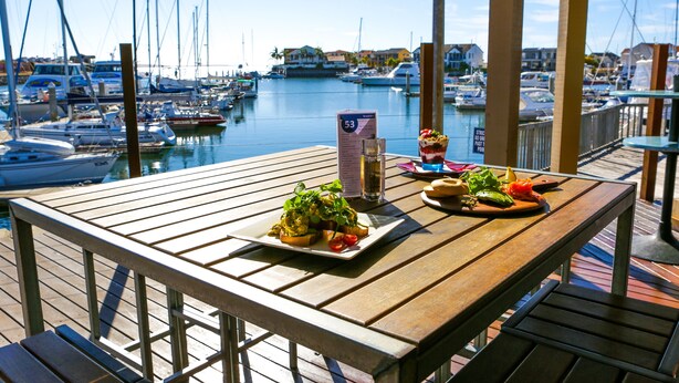 A wooden deck with a table set for a meal, overlooking a marina with boats. - The Marina Hotel (Port Lincoln)
