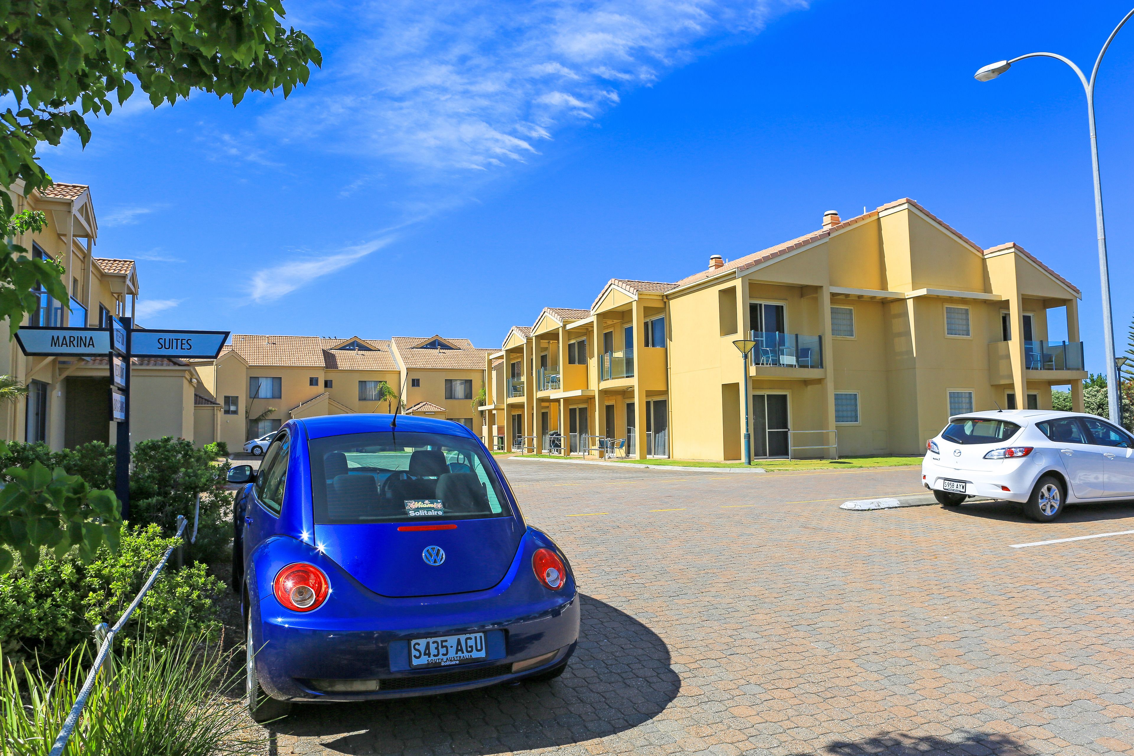 Un'auto blu Volkswagen parcheggiata di fronte a un edificio giallo con cartelli che indicano 'Marina' e 'Suites'.