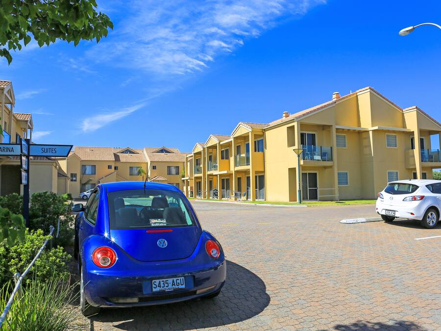 Un'auto blu Volkswagen parcheggiata di fronte a un edificio giallo con cartelli che indicano 'Marina' e 'Suites'.