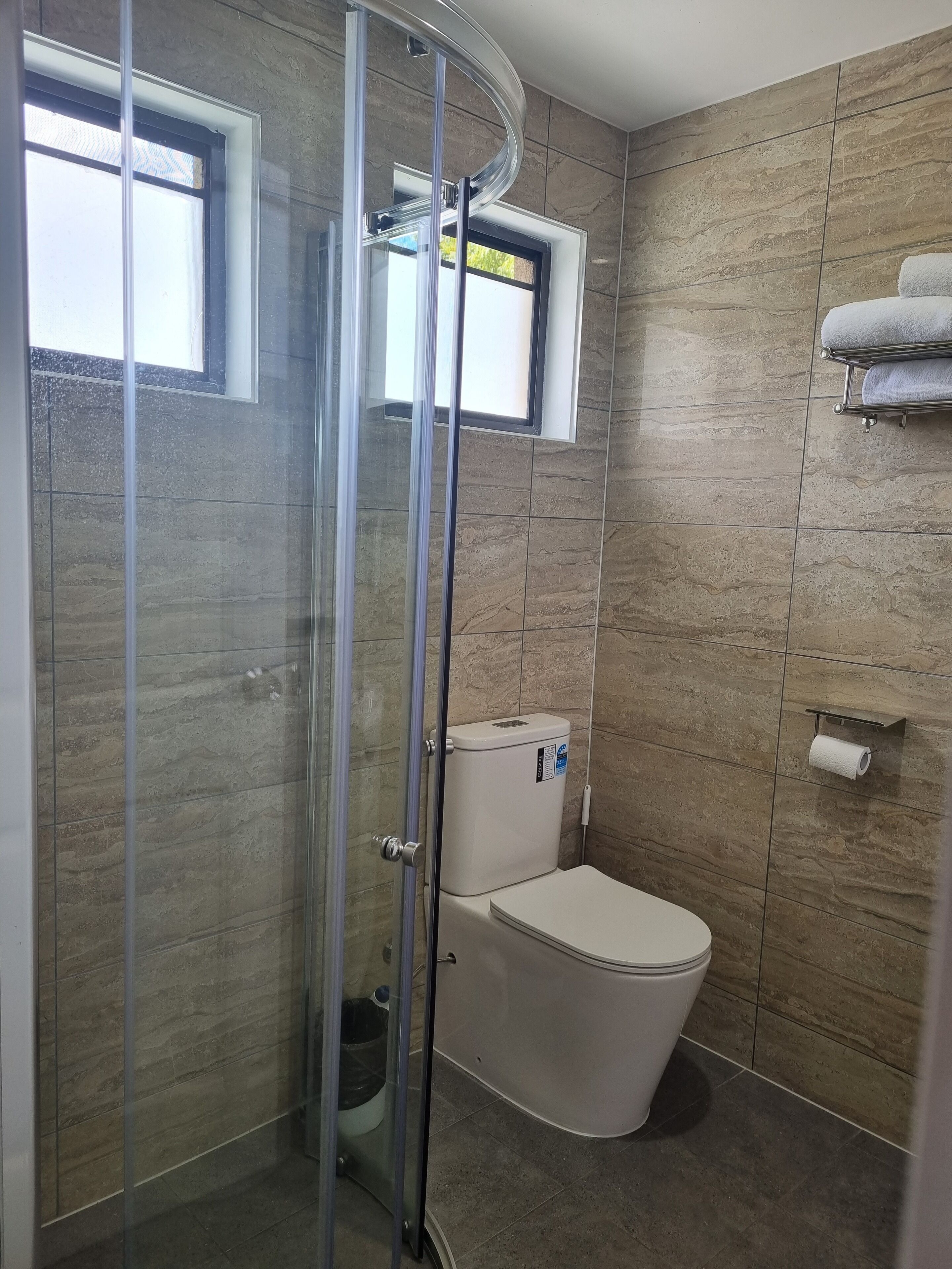 A bathroom with a glass shower enclosure, a toilet, and a towel rack.