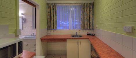 A compact kitchen with a sink, a microwave, and a window with curtains.