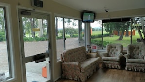 A reception area with a closed door, two floral armchairs, a television, and a view of the outdoors. - All Seasons Country Lodge (Taree South)