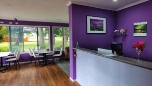 A reception area with a purple wall, a reception desk, and a seating area with chairs and a table. - All Seasons Country Lodge (Taree South)