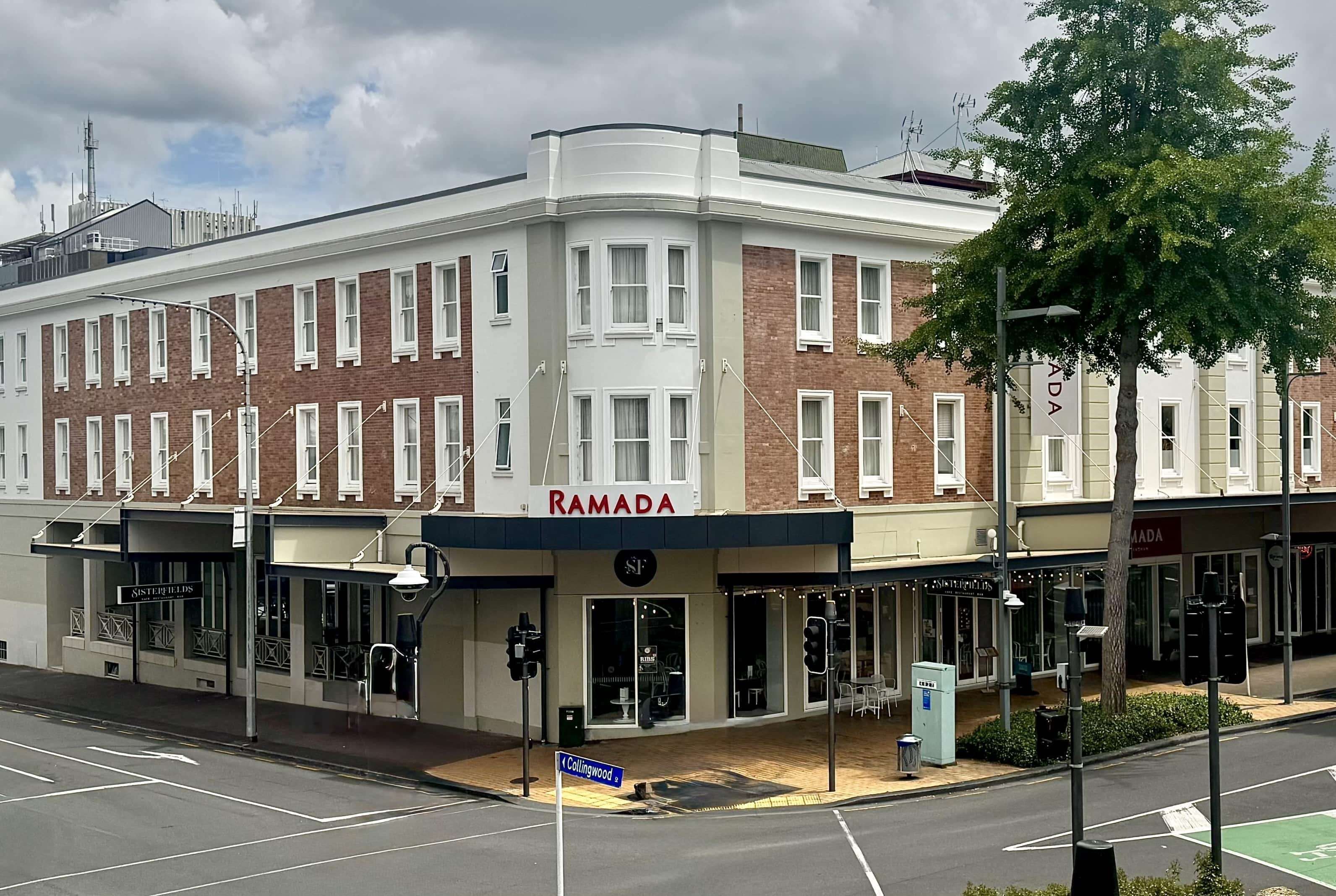 A corner building with a 'RAMADA' sign, storefronts, and a street sign for 'Collingwood St.'