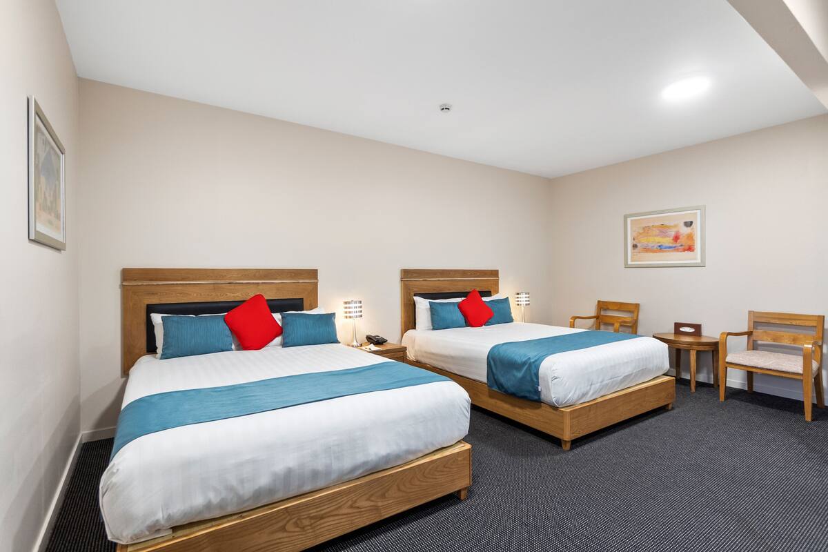 A hotel room with two beds, a desk, a chair, and a small table.