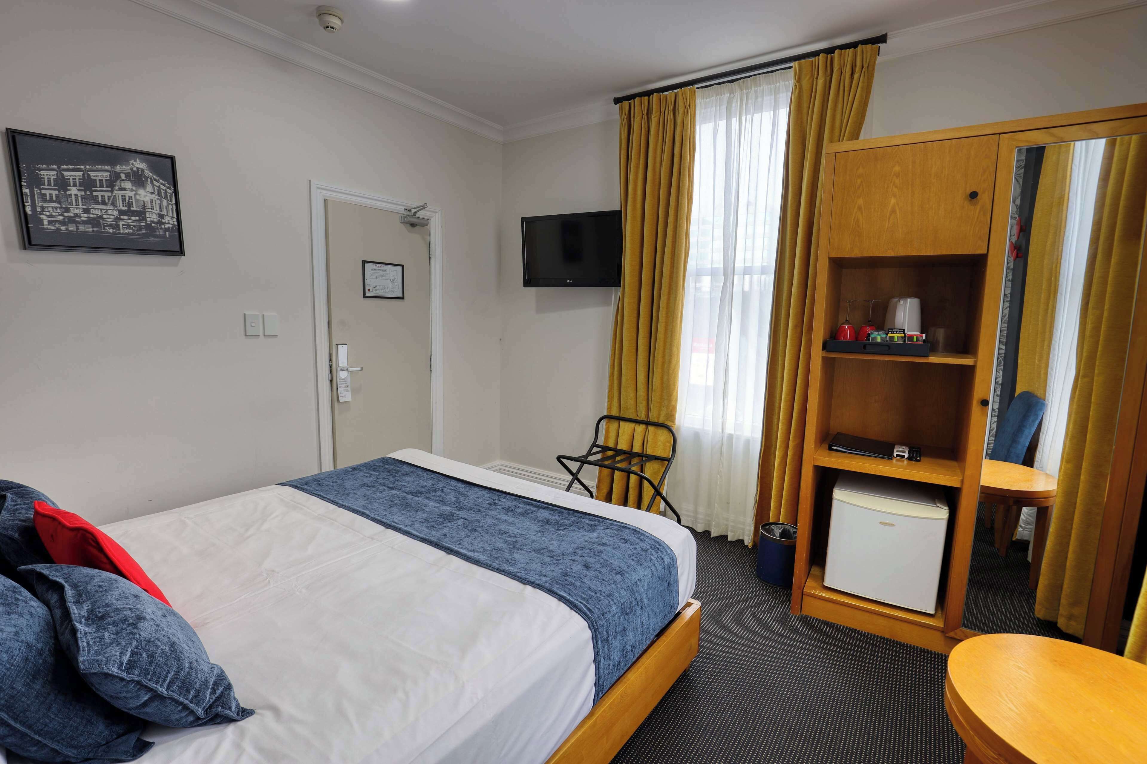 A hotel room with a bed, a television, a wardrobe, and a small table.