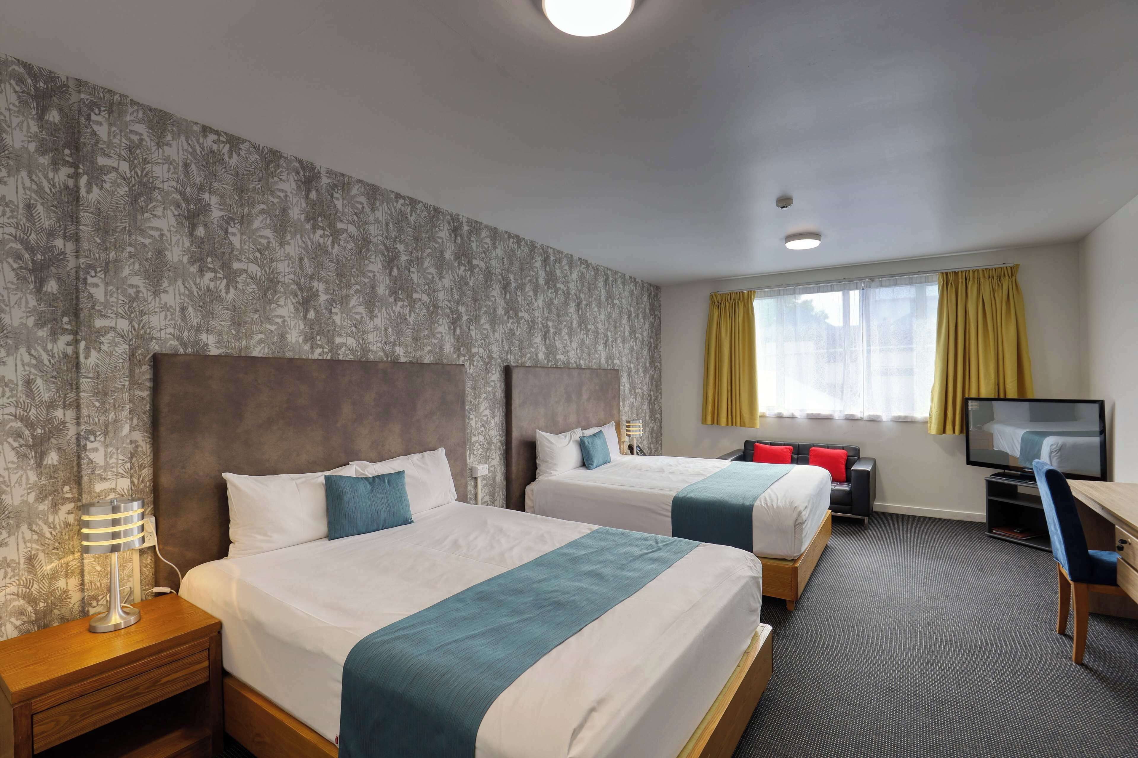 A hotel room with two beds, a desk, a TV, and a window with curtains.
