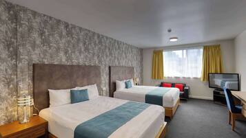 A hotel room with two beds, a desk, a TV, and a window with curtains.