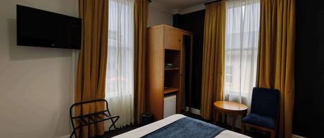 A hotel room with a bed, a TV mounted on the wall, a small desk, a chair, and a wardrobe.