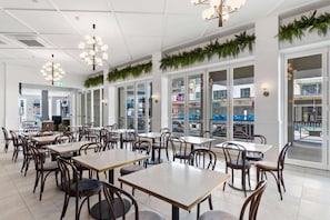 A spacious indoor dining area with multiple tables and chairs, large windows, and decorative greenery. - Ramada by Wyndham Hamilton City Center (Hamilton)