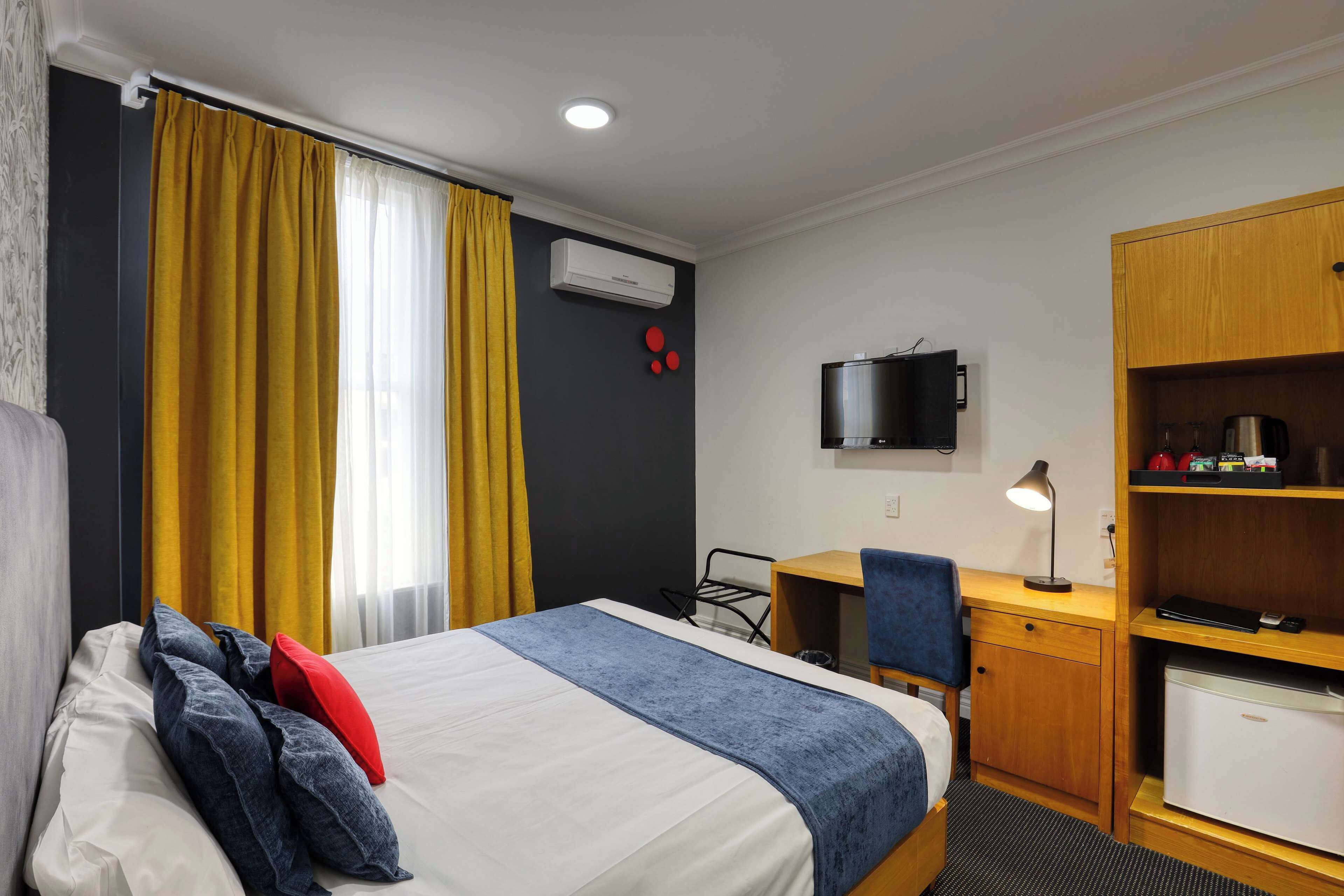 A hotel room with a bed, a desk, a chair, a TV, a mini-fridge, and a wardrobe.