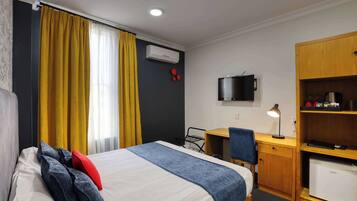 A hotel room with a bed, a desk, a chair, a TV, a mini-fridge, and a wardrobe.
