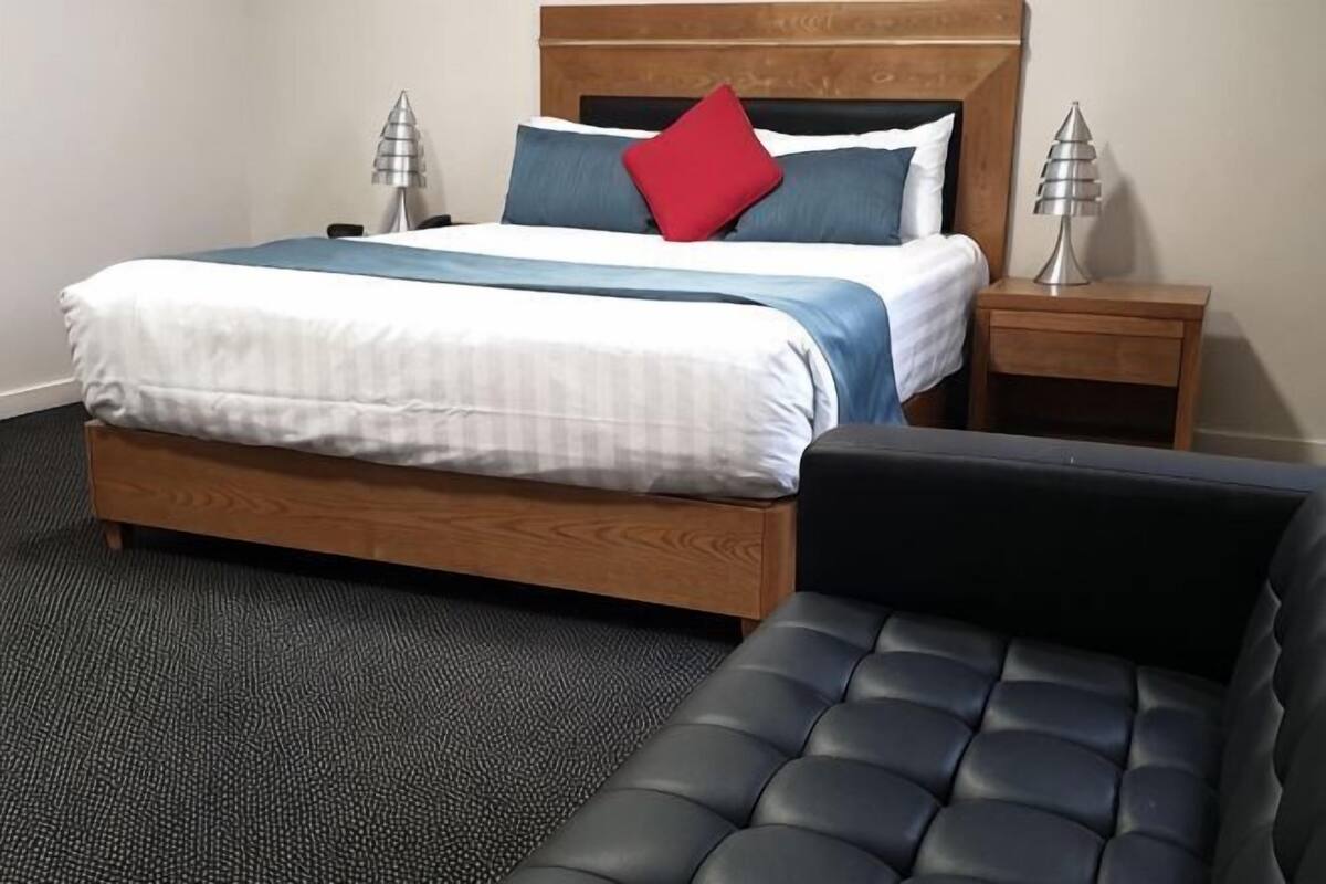 A bedroom with a bed, bedside tables, and a black leather sofa.