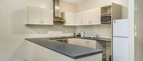 A compact kitchen with a central island, white cabinets, a stainless steel range hood, a microwave, and a refrigerator.