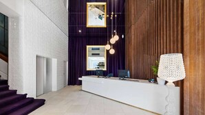 A reception area with a white reception desk, purple curtains, and a wooden panel wall. - Ramada by Wyndham Hamilton City Center (Hamilton)