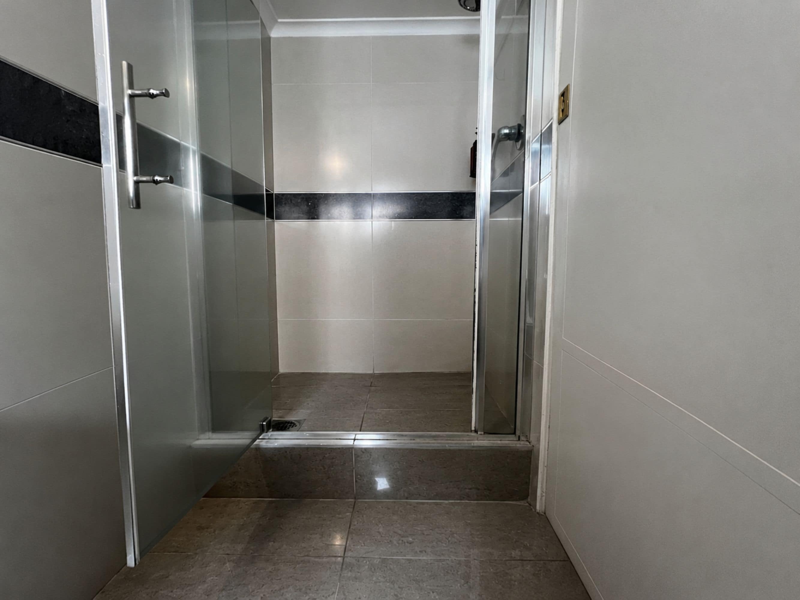 A glass-enclosed shower stall with a tiled floor and a metallic handle.
