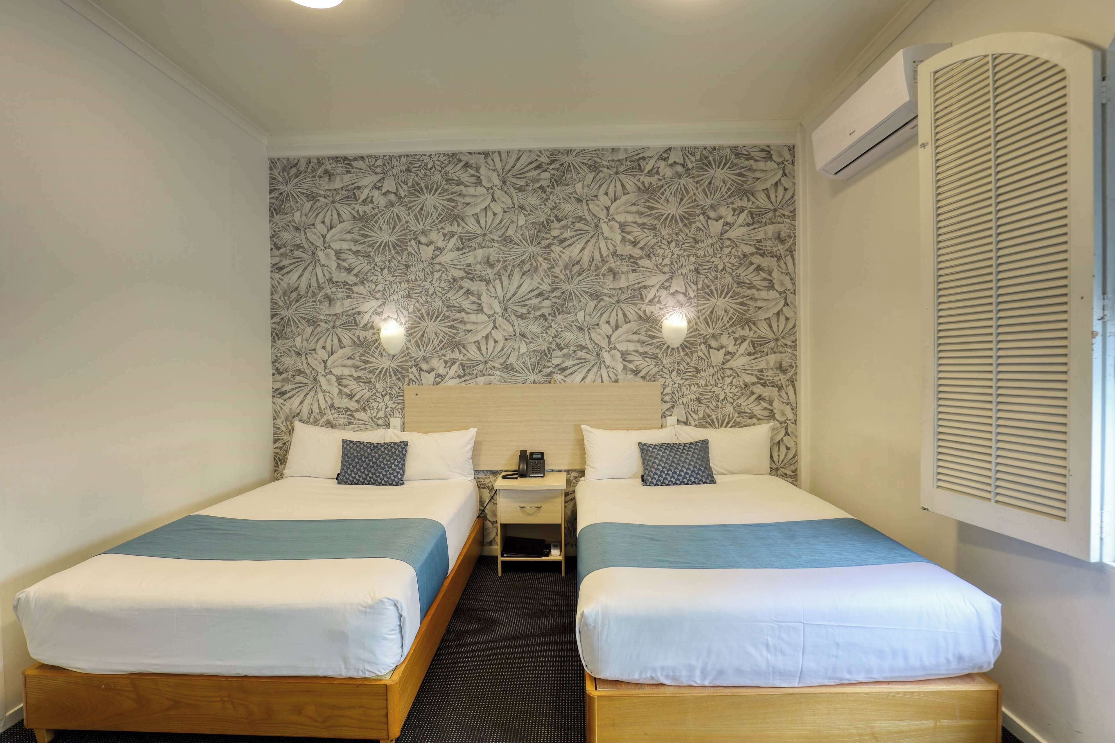 A double room with two beds, a nightstand, a phone, and a wall-mounted air conditioner.