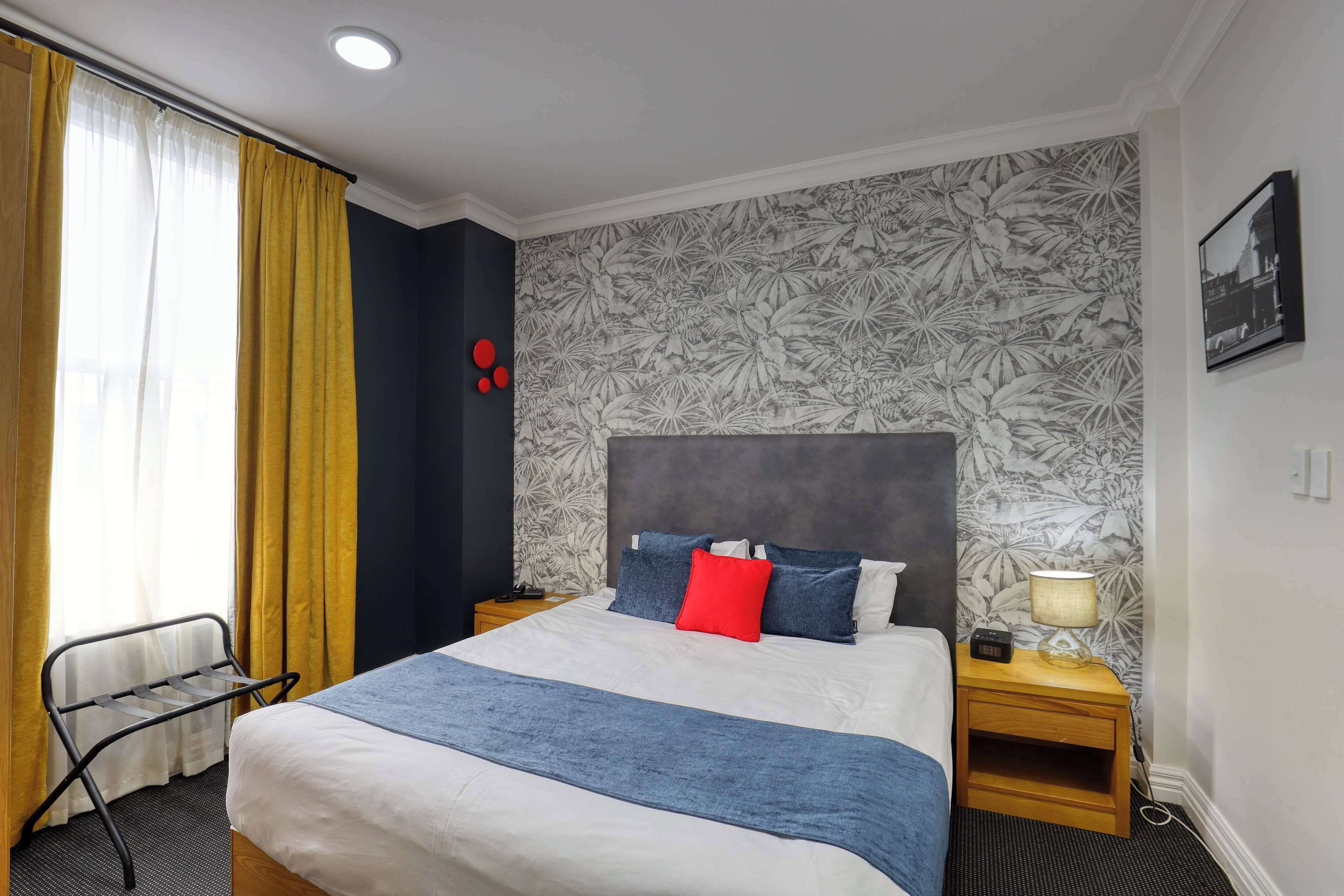 Une chambre d’hôtel avec un lit, une table de chevet, une chaise et une fenêtre avec des rideaux.
