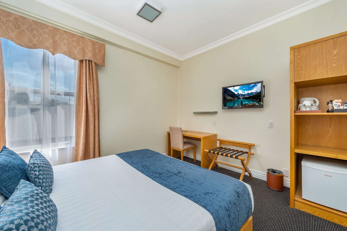 A hotel room with a bed, a desk, a chair, a television, and a small refrigerator.