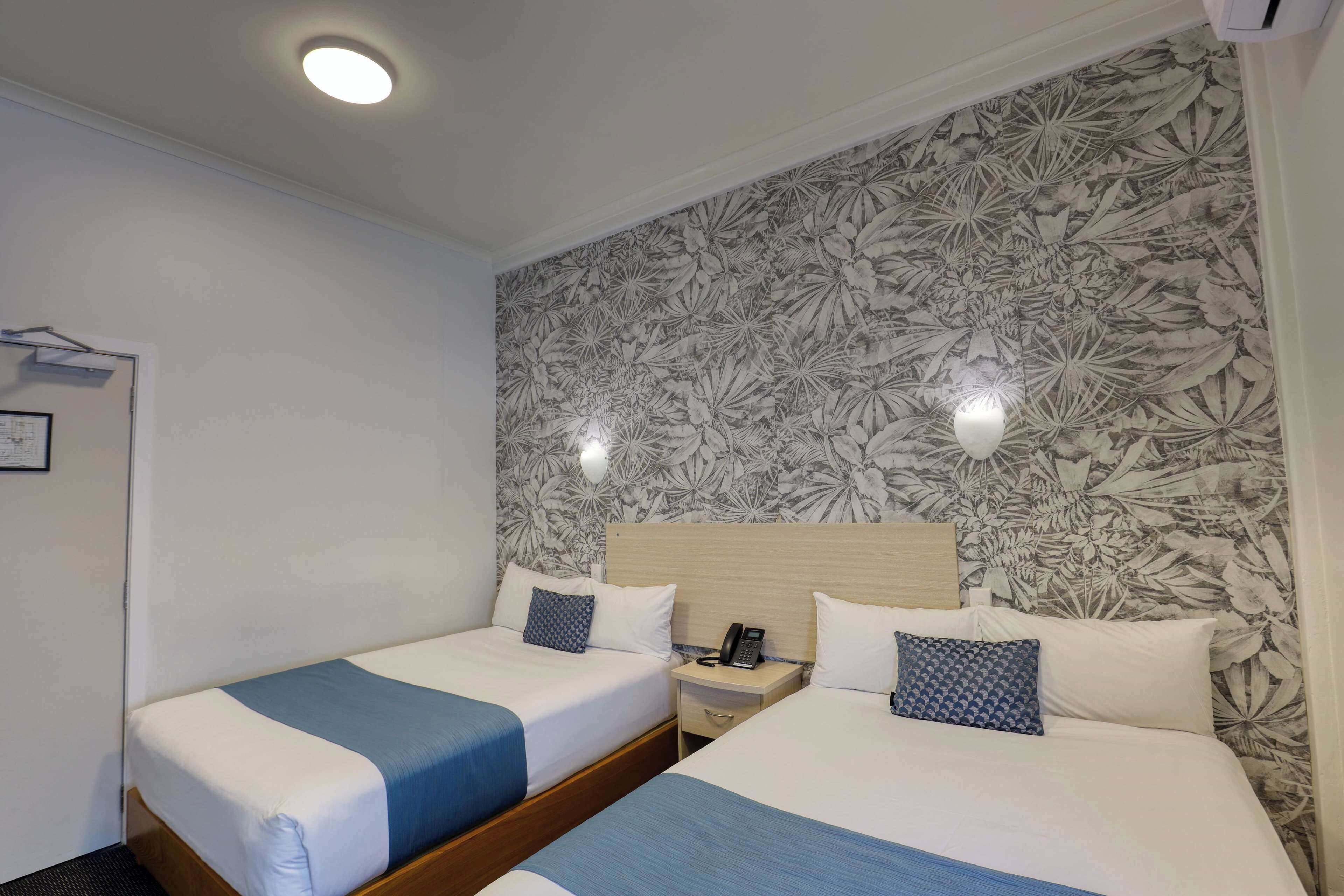 Ein Hotelzimmer mit zwei Betten, einem Nachttisch mit Telefon und einer Wand mit Blumenmuster.