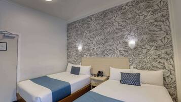 Ein Hotelzimmer mit zwei Betten, einem Nachttisch mit Telefon und einer Wand mit Blumenmuster.