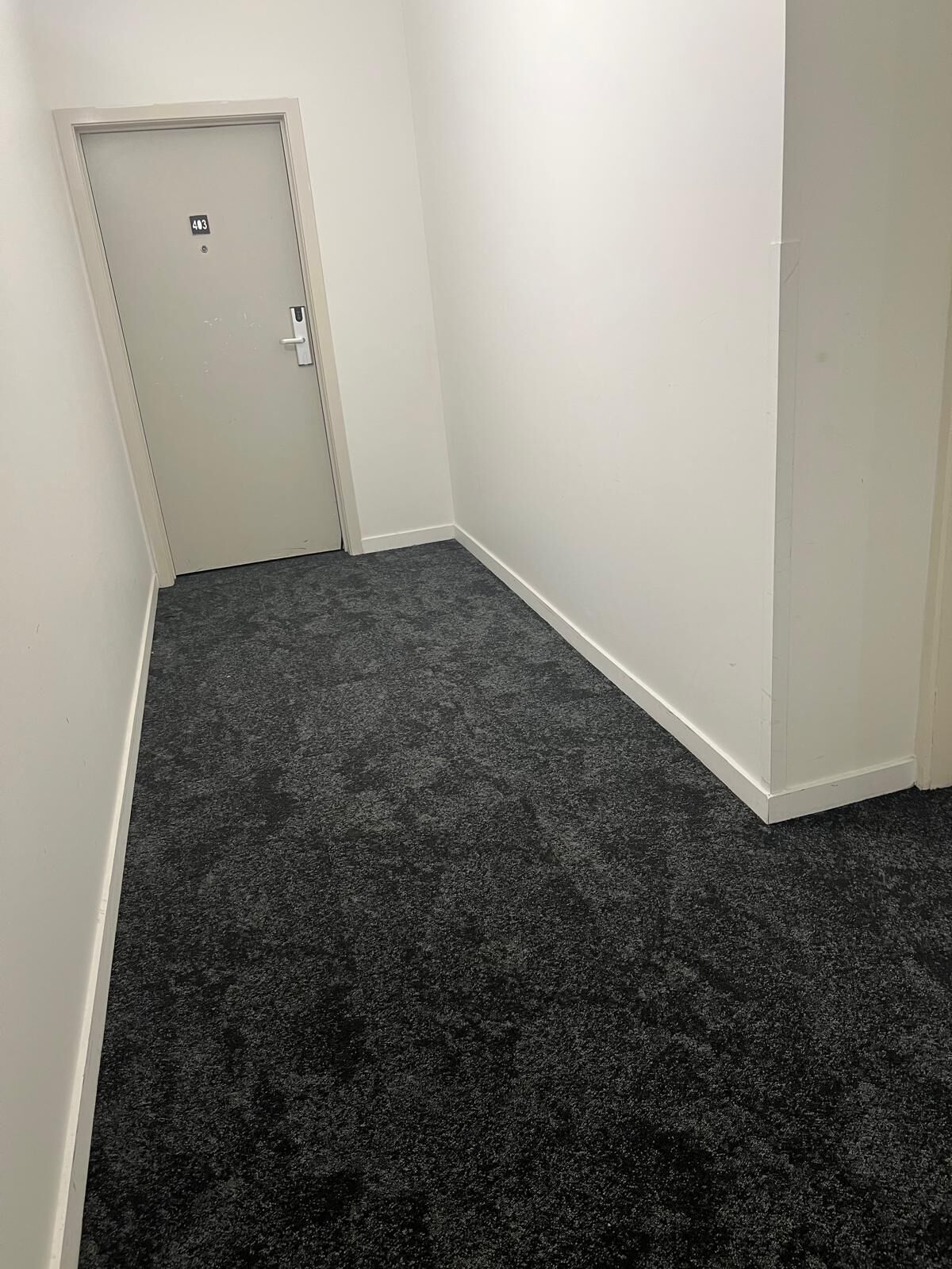 Ein kleiner, leerer Raum mit dunklem Teppich, weißen Wänden und einer Tür mit einer Nummer.