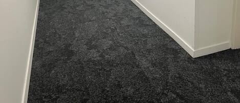 A small, empty room with a dark carpet, white walls, and a door with a number plate.