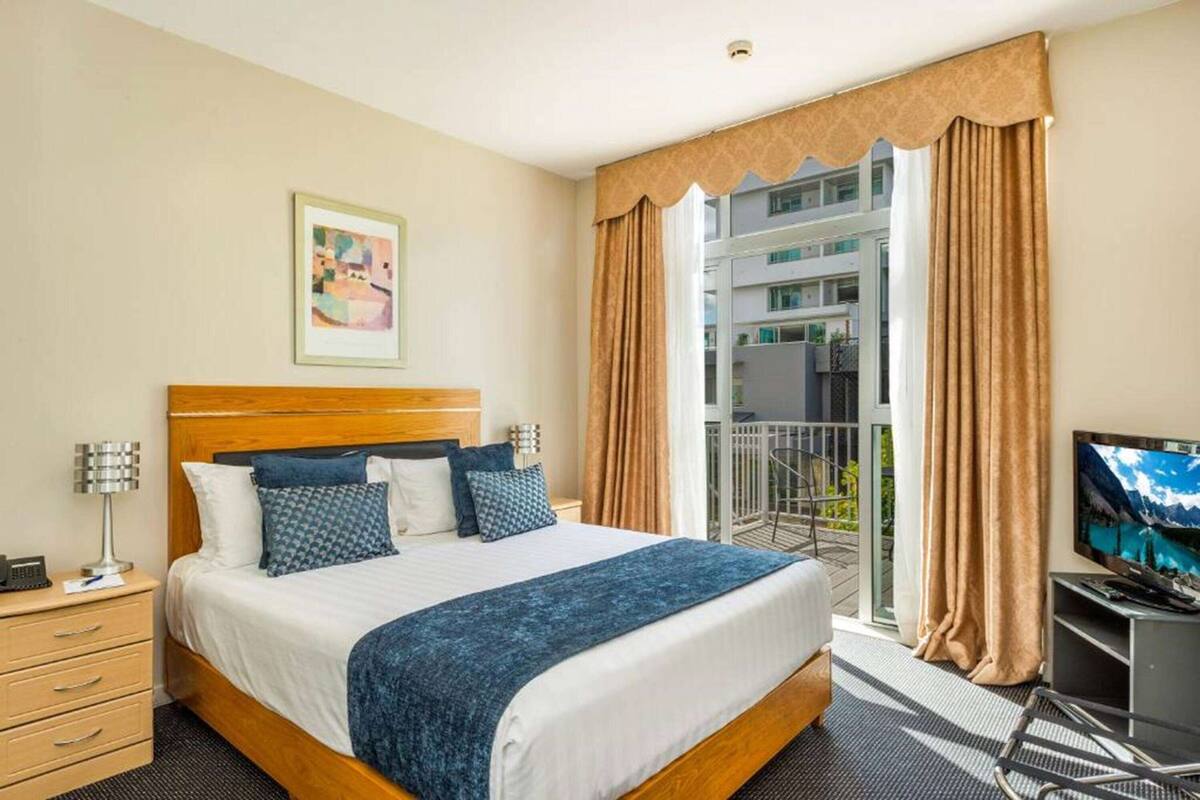 A hotel room with a large bed, a desk, a television, and a balcony with curtains.