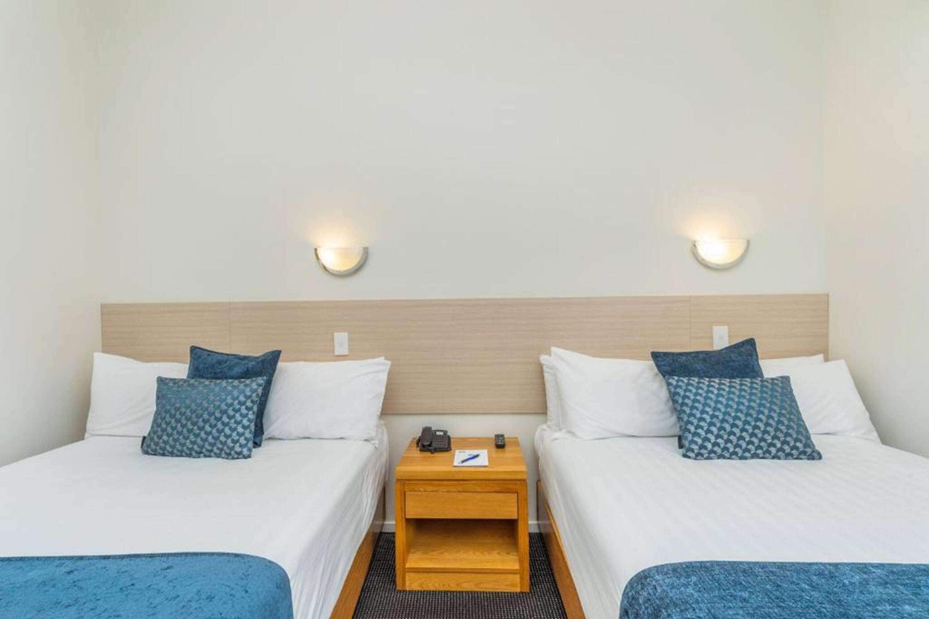A hotel room with two beds, a wooden nightstand, and wall-mounted lights.