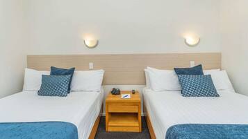 A hotel room with two beds, a wooden nightstand, and wall-mounted lights.
