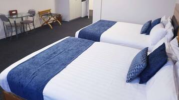 A hotel room with two beds, a desk, chairs, and a small kitchenette.