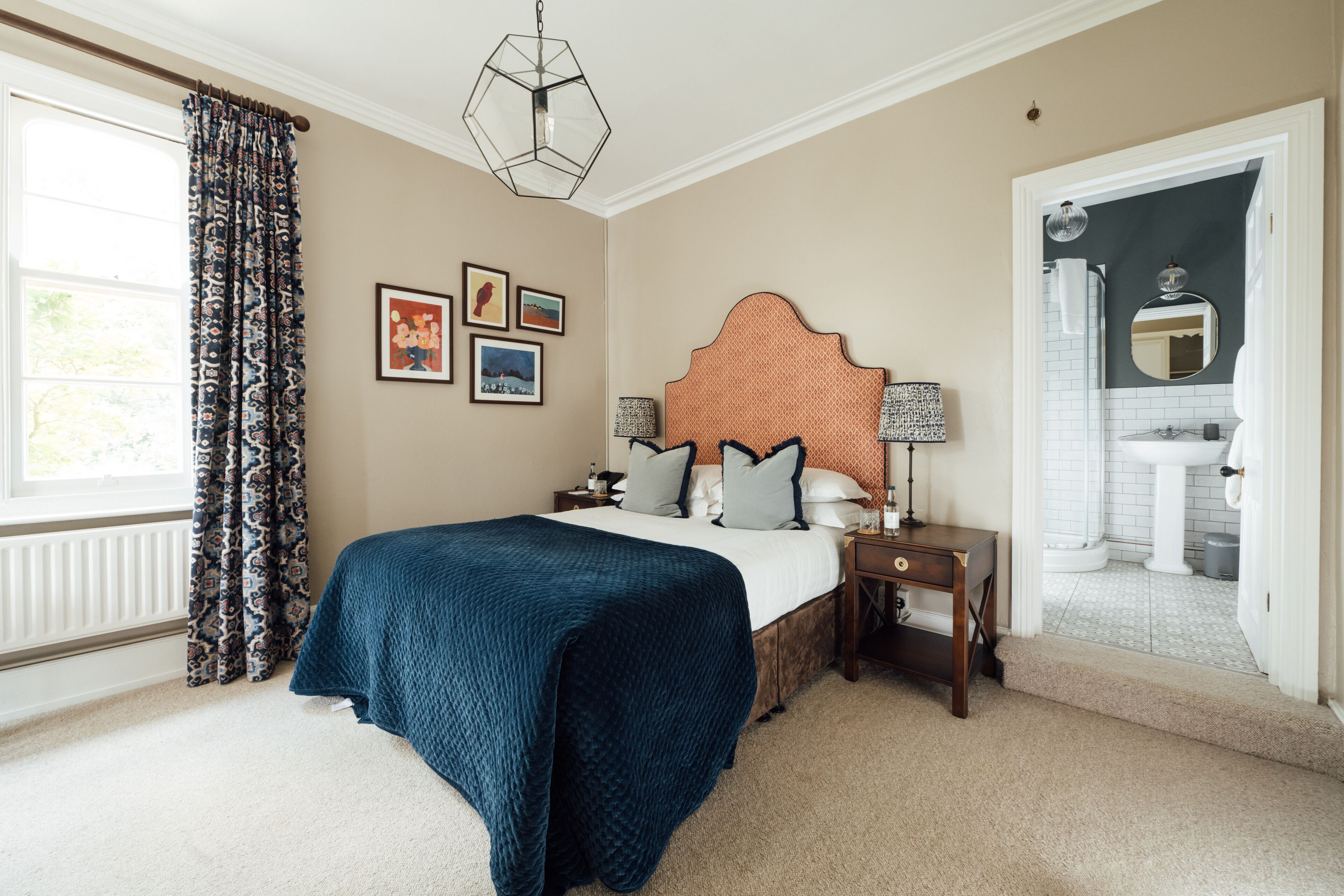 A bedroom with a large bed, a nightstand, a dresser, and a window with curtains.